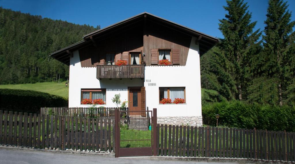 een wit huis met een zwart dak en een hek bij La Casetta nelle Dolomiti in Perarolo di Cadore