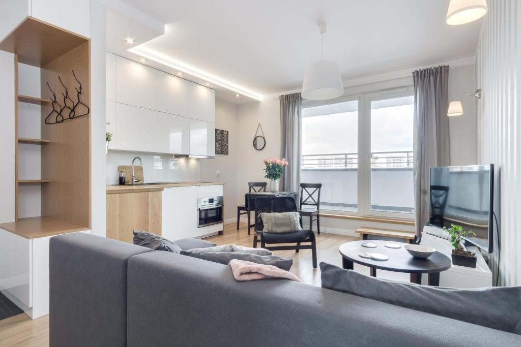 a living room with a grey couch and a kitchen at Elite Apartments Marine Suite in Gdańsk