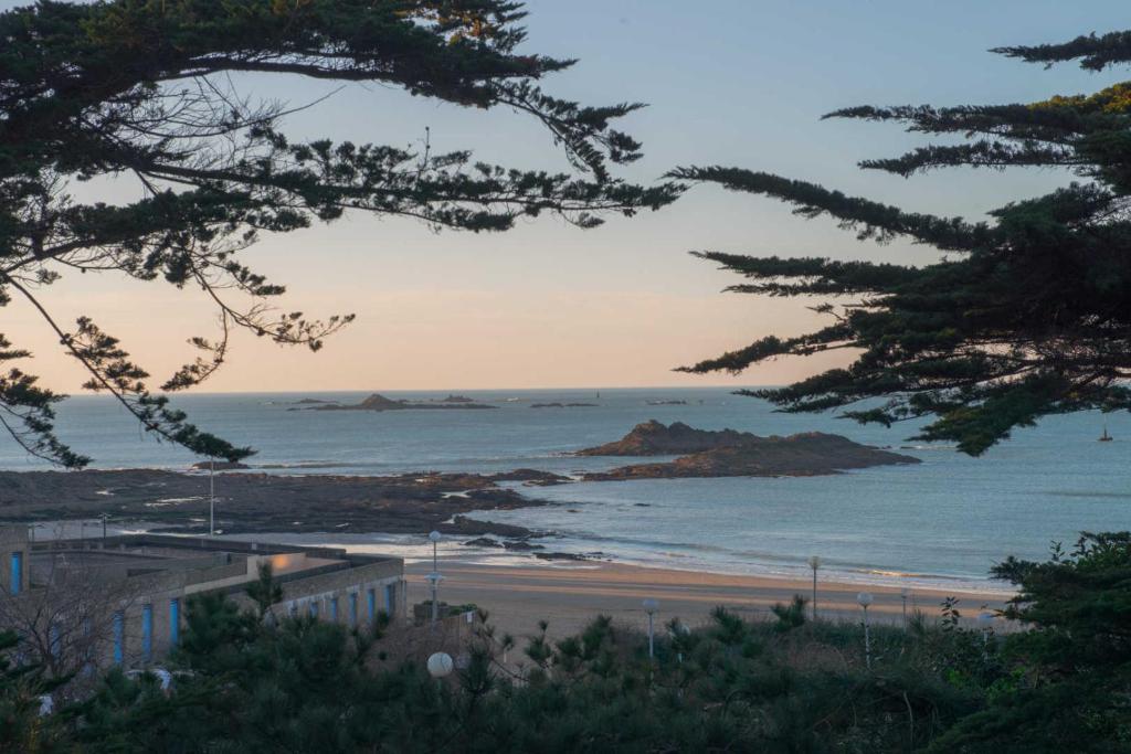 Blick auf den Strand von einem Hügel mit Bäumen in der Unterkunft la Pinède in Dinard