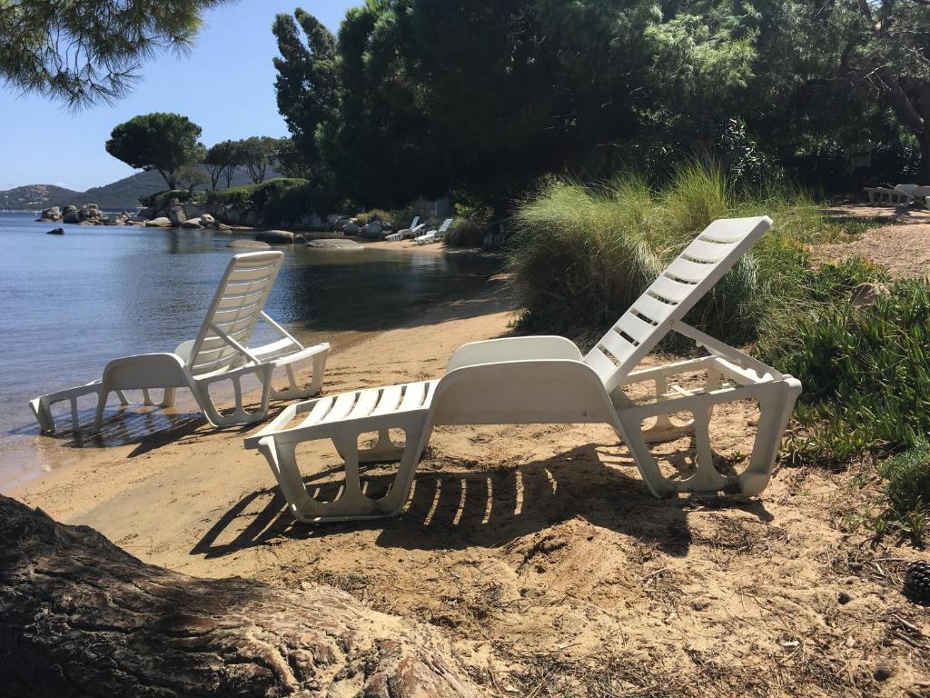 2 chaises blanches assises sur une plage au bord de l'eau dans l'établissement Résidence les pieds dans l'eau, à Porto-Vecchio