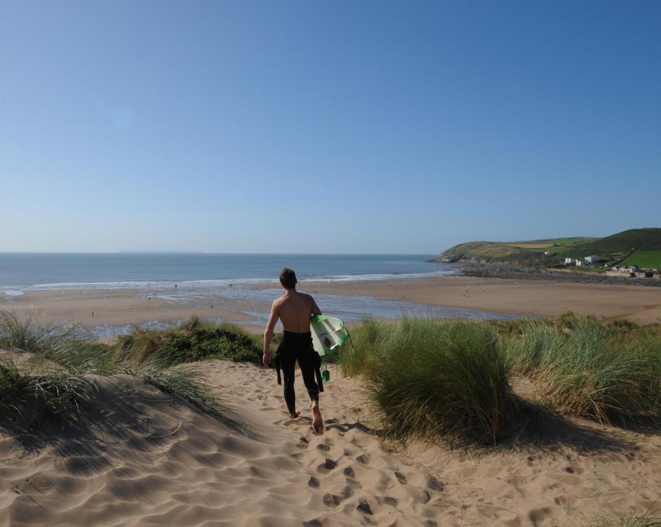 a man walking down a sandy beach with a surfboard at Croyde Bay Hotel or Self Catering in Croyde