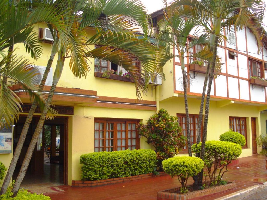um edifício amarelo com palmeiras em frente em Hosteria Los Helechos em Porto Iguaçu