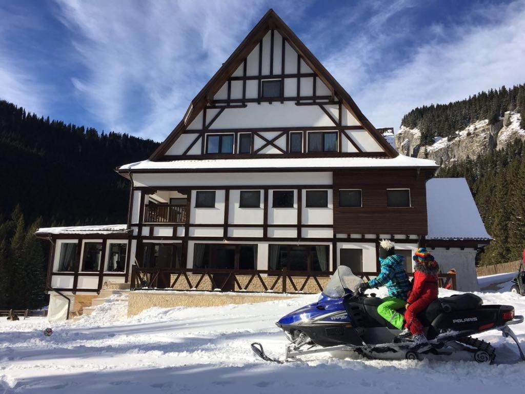 twee mensen op een sneeuwscooter voor een huis bij Chalet Alpina in Moroeni