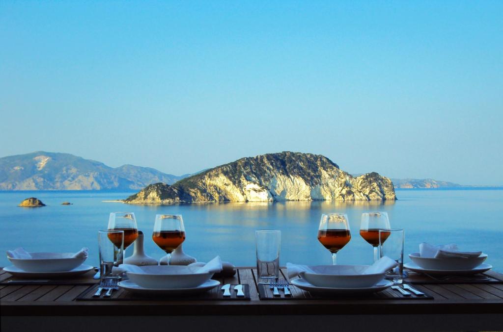 una mesa con copas de vino y vistas al océano en Exensian Villas & Suites, en Marathias