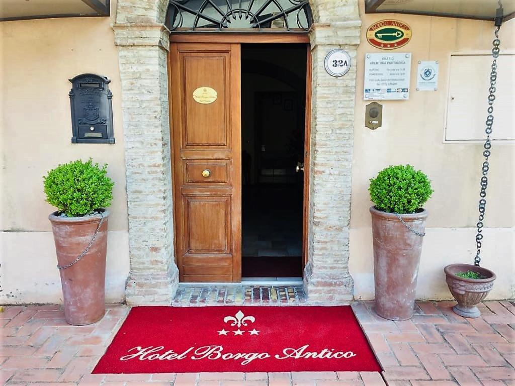 a red mat in front of a door with two potted plants at Hotel Borgo Antico in Fabriano