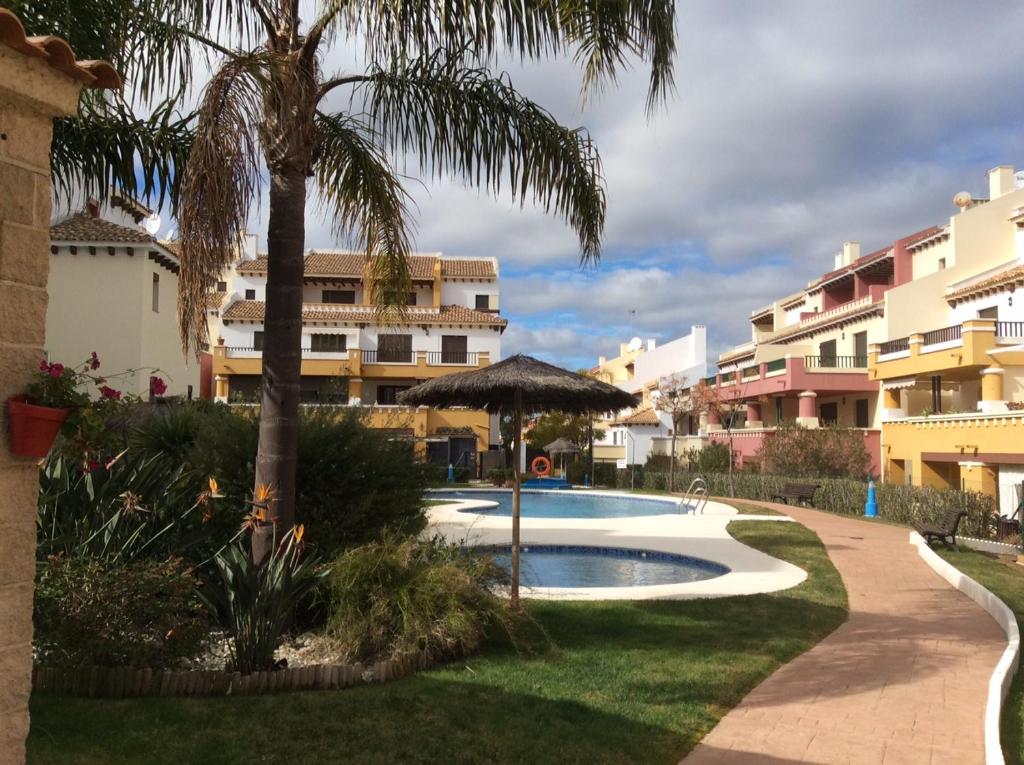 a swimming pool with an umbrella and some buildings at Costa Esuri Ayamonte Apartment in Ayamonte