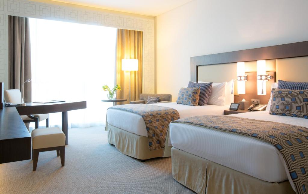 a hotel room with two beds and a desk at Royal M Hotel Fujairah by Gewan in Fujairah