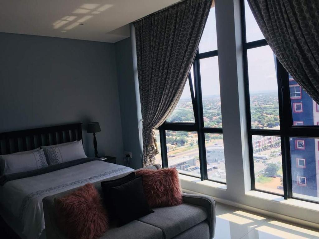 ein Schlafzimmer mit einem Bett und einem Sofa sowie großen Fenstern in der Unterkunft Pat Luxurious Studio in Gaborone