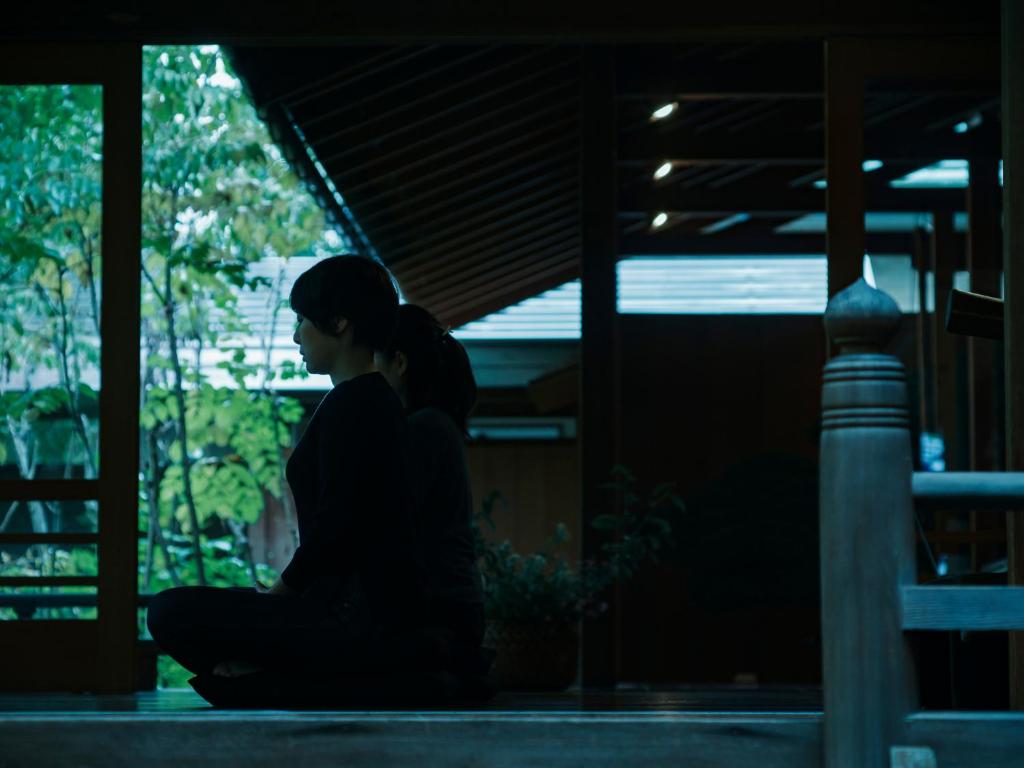 uma mulher sentada no chão num quarto escuro em ZEN&BED Bogetsu-An em Koshu