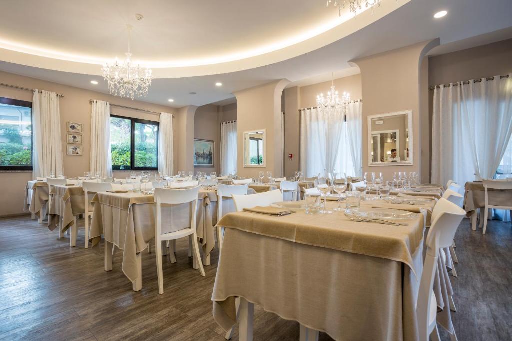 a dining room with tables and chairs and chandeliers at Hotel Corallo in Milano Marittima