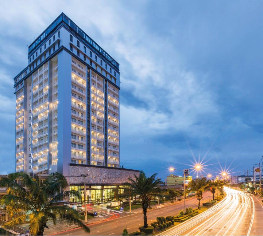 a tall blue building with palm trees in front of a street at Kantary Hotel Korat in Nakhon Ratchasima