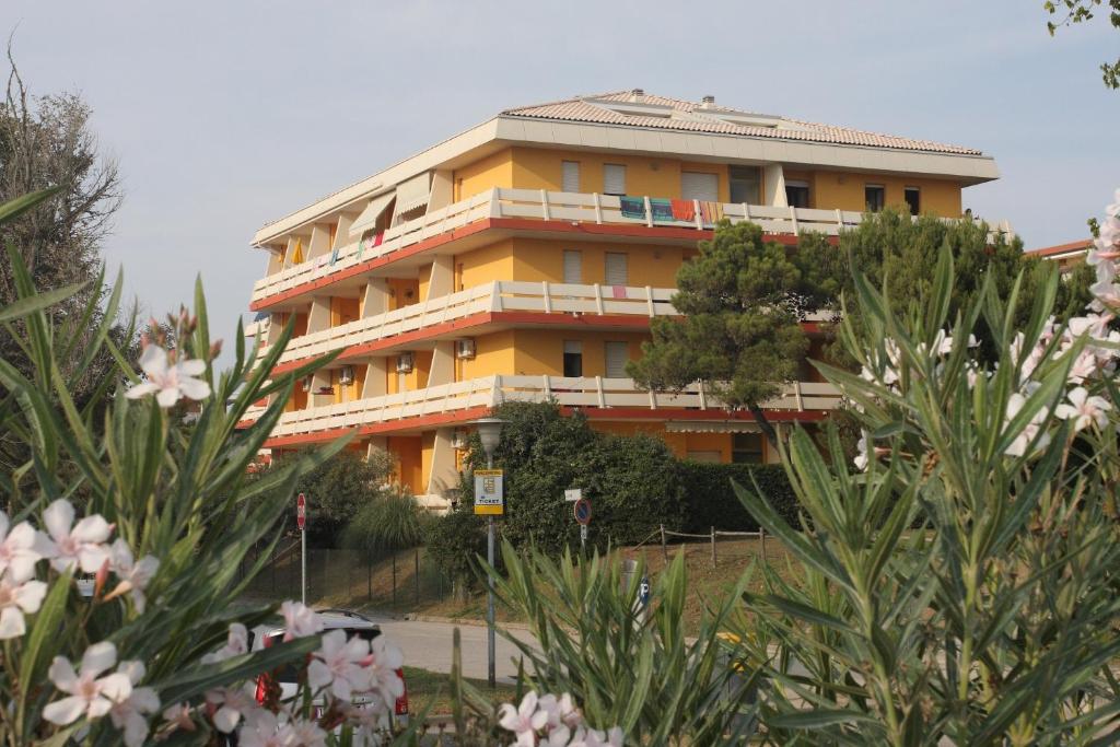 un bâtiment jaune avec des arbres devant lui dans l'établissement Condominio Carina, à Bibione