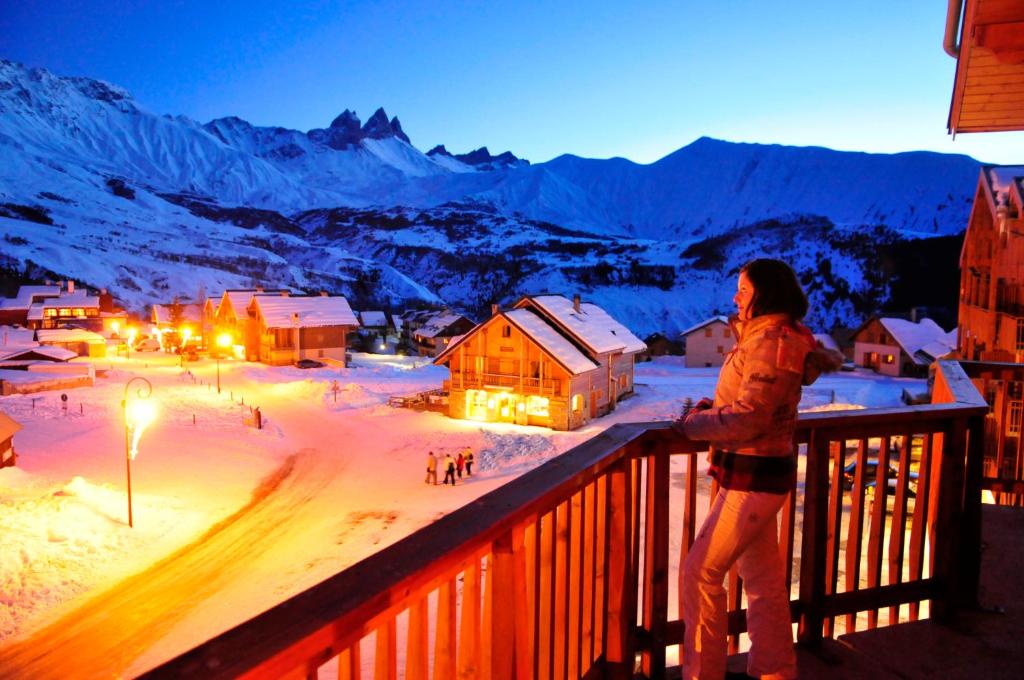 a woman standing on a balcony overlooking a snow covered village at Résidence Goélia Le Relais des Pistes in Albiez-le-Vieux