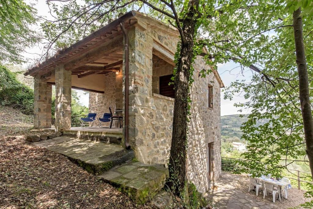 uma casa de pedra na floresta com uma mesa e cadeiras em La villa della quercia em Seggiano