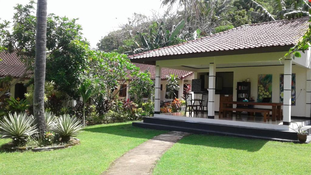a small house with a porch and a green yard at Indah Homestay and Cooking classes in Senggigi