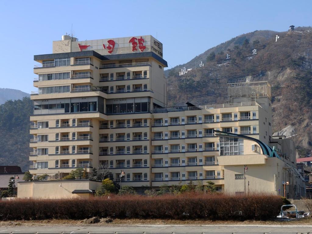 a large white building in front of a mountain at Riverside Uedakan in Chikuma