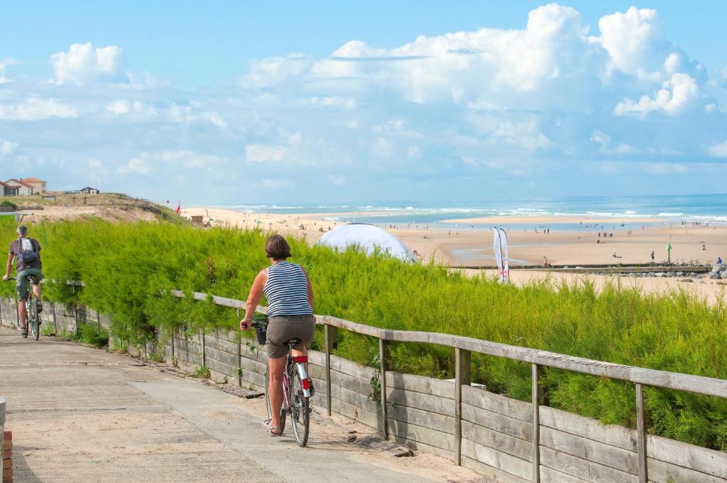 two people riding bikes down a path near the beach at Résidence Goélia Les Jardins de l'Oyat in Mimizan-Plage