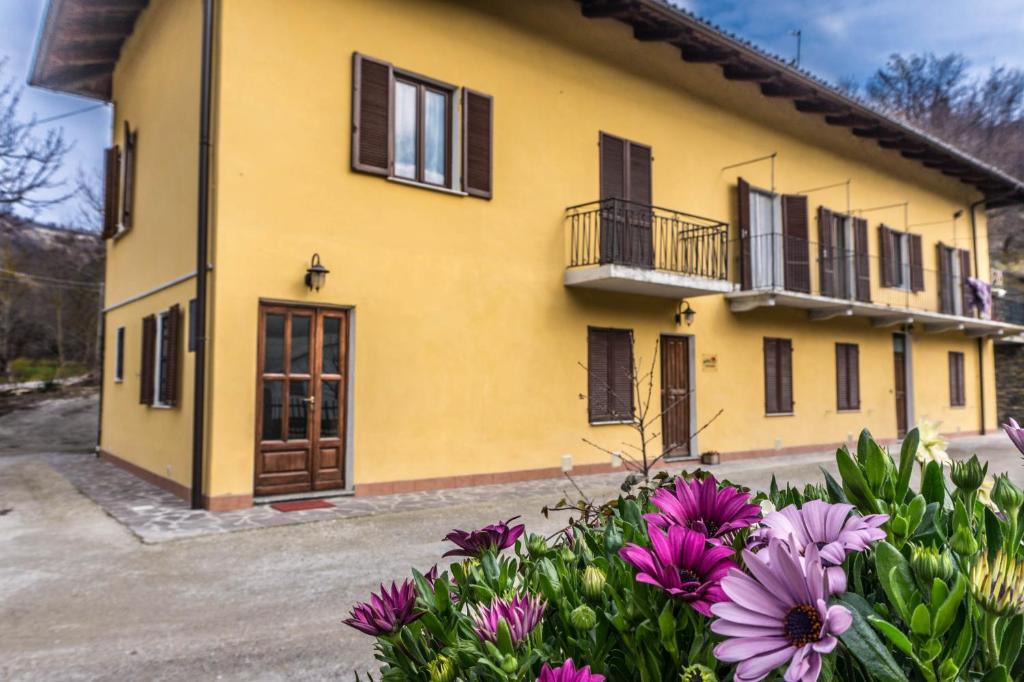 uma casa amarela com janelas pretas e flores roxas em Casa in Langa em Alba