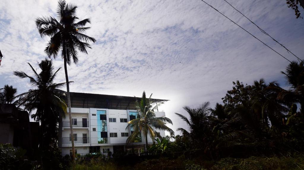 a building with palm trees and a cloudy sky at Indeevaram Residency in Trivandrum
