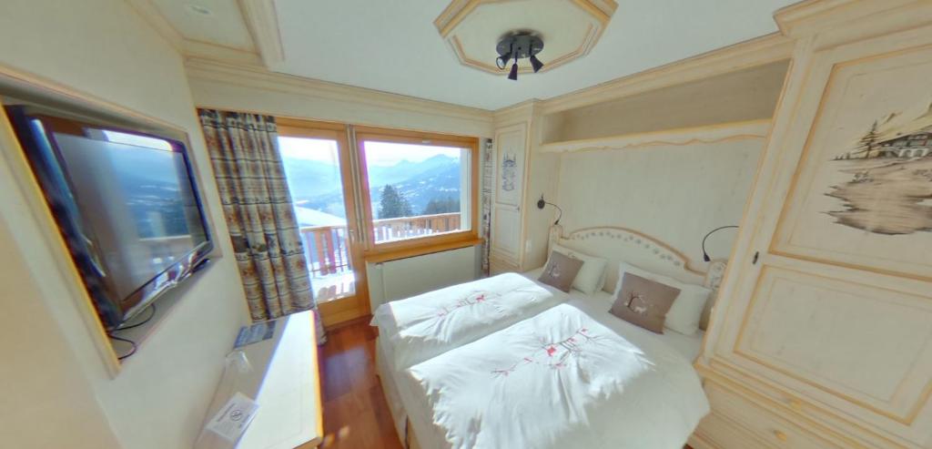 1 dormitorio con 1 cama, TV y ventana en Les Petits Mélèzes, en Crans-Montana