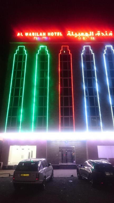 Al Mabila Hotel في سيب: مبنى مضاء فيه سيارات متوقفة أمامه