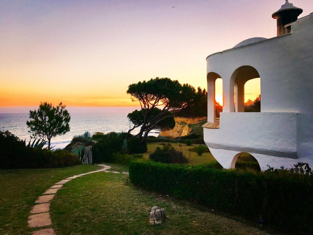 una puesta de sol sobre el océano con una casa blanca en E&M Beach House Aldeamento do Levante I, en Armação de Pêra
