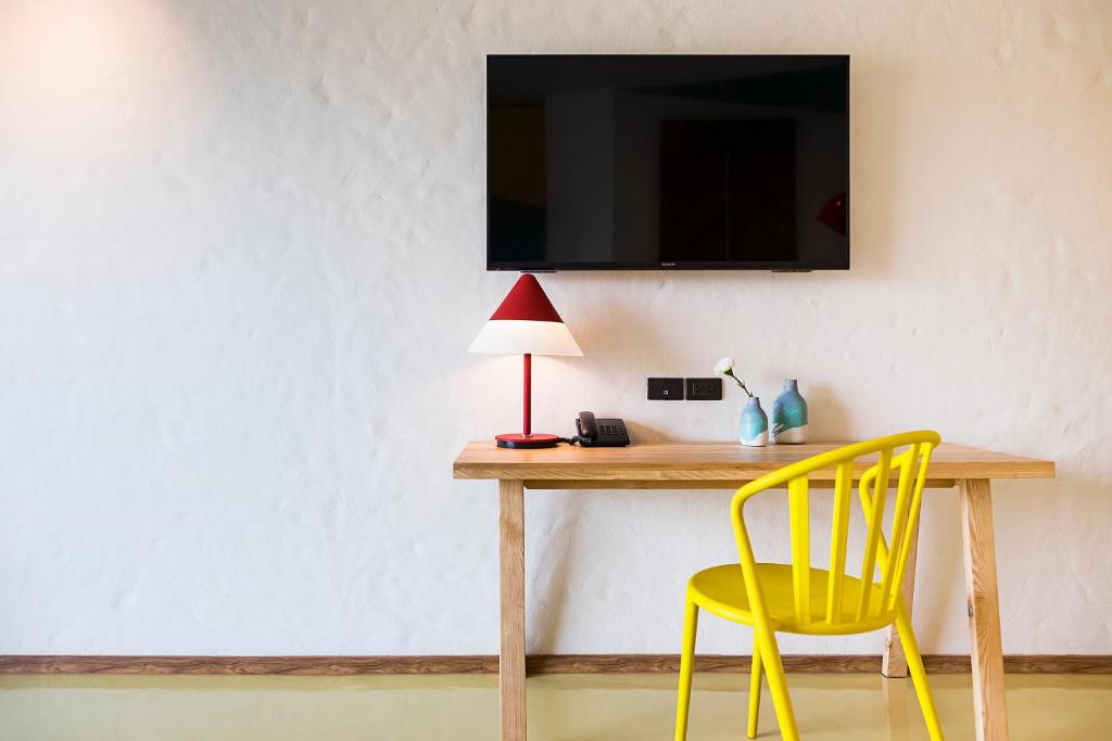 A compact wooden desk with a bright yellow chair, lamp and wall-mounted television.