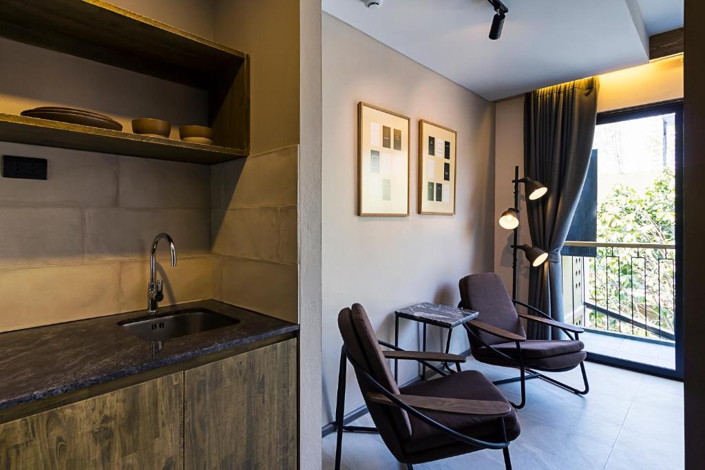 A studio corner with a kitchenette, two lounge chairs and a balcony-facing glass door.