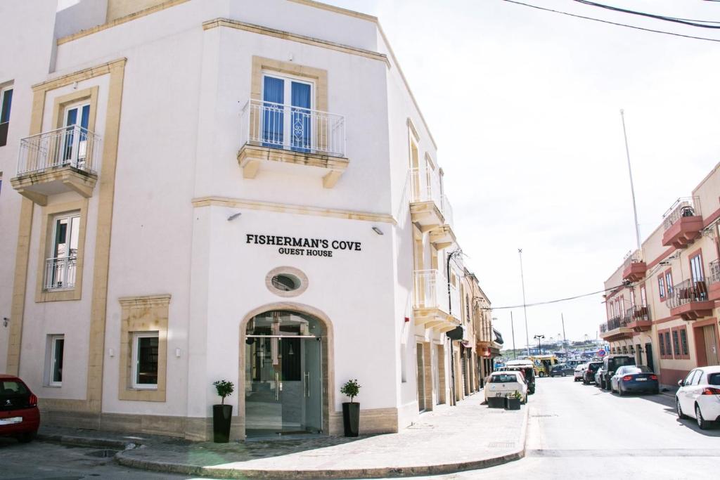 un edificio bianco su una strada con auto parcheggiate di Fisherman's Cove Guesthouse a Marsaxlokk