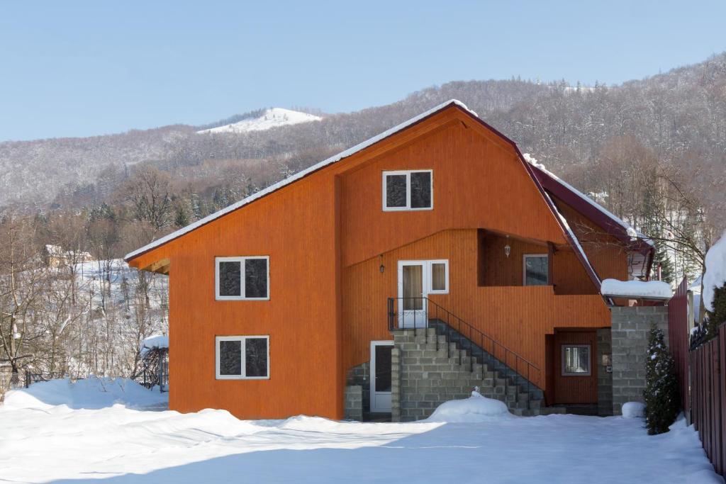 une maison orange avec de la neige devant elle dans l'établissement Акорди Плеса, à Yaremtche
