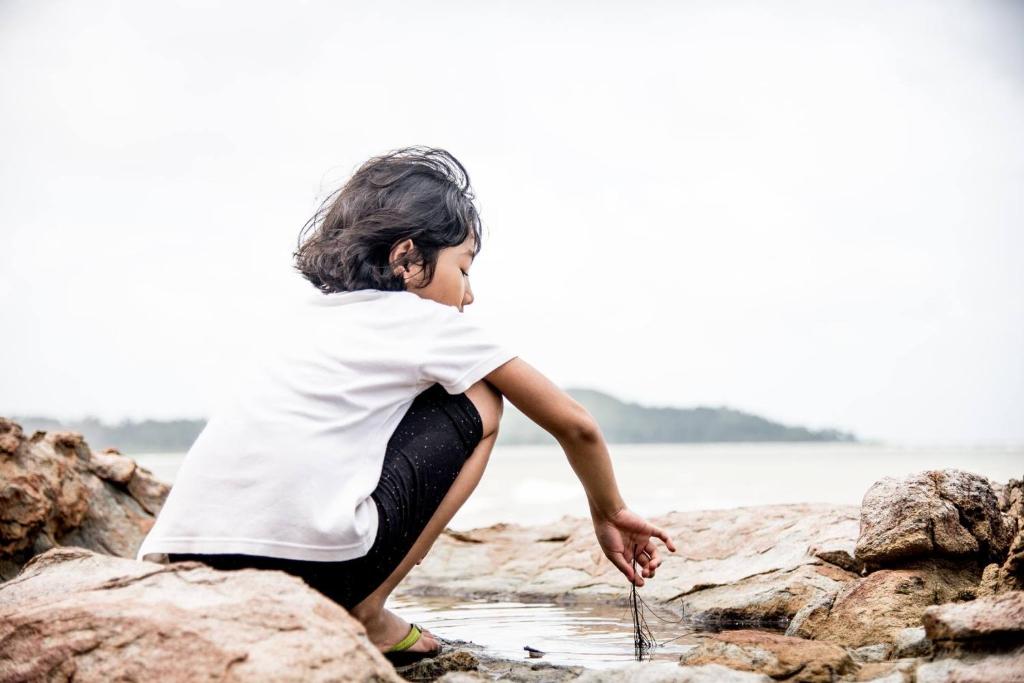 a young child sitting on rocks at the beach at Pandan Beach Homestay in Kampong Pandan