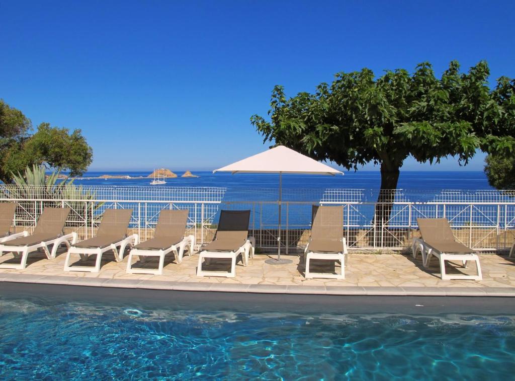 a group of chairs and an umbrella next to a swimming pool at Résidence Marine de Palumbare in LʼÎle-Rousse