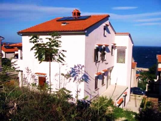 a white house with a red roof and the ocean at Apartment Budinic in Mali Lošinj