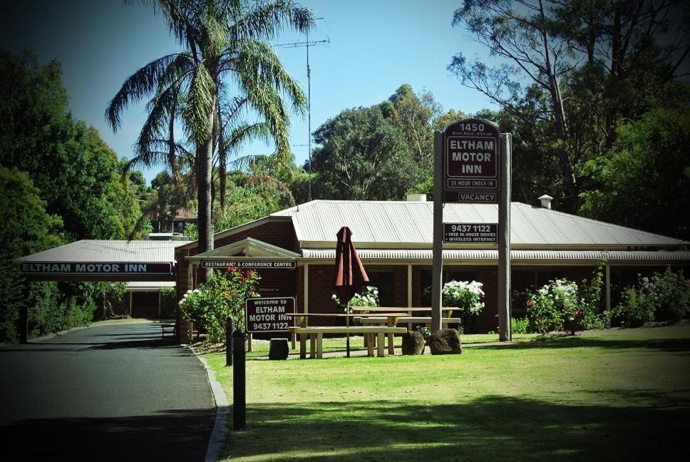 a woman sitting on a bench in front of a palm tree at Eltham Motor Inn in Eltham