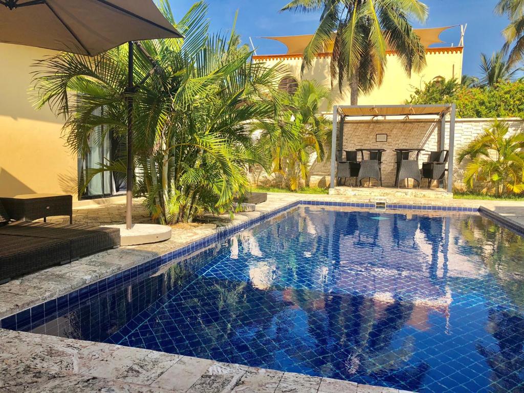 a swimming pool with an umbrella next to a house at Grand Amber Villa in Diani Beach