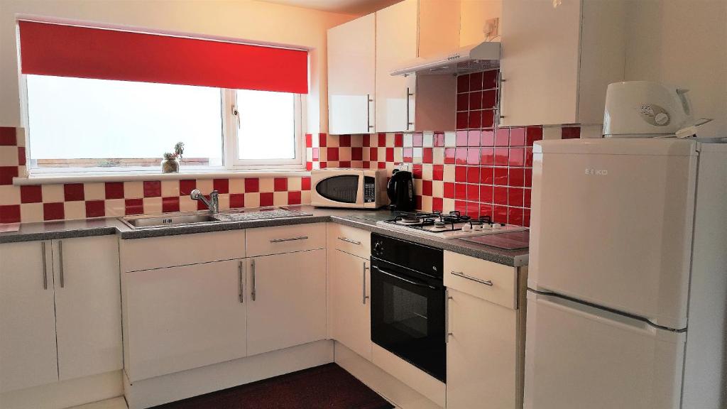 una cocina con armarios blancos y una pared de azulejos rojos en Swindon Old Town Studio - EnterCloud9SA, en Swindon