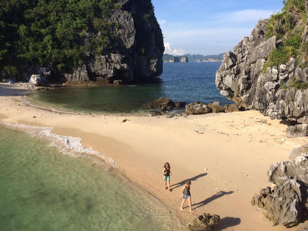 2 persone che camminano su una spiaggia con una tavola da surf di Nhat Mai Hotel a Cat Ba