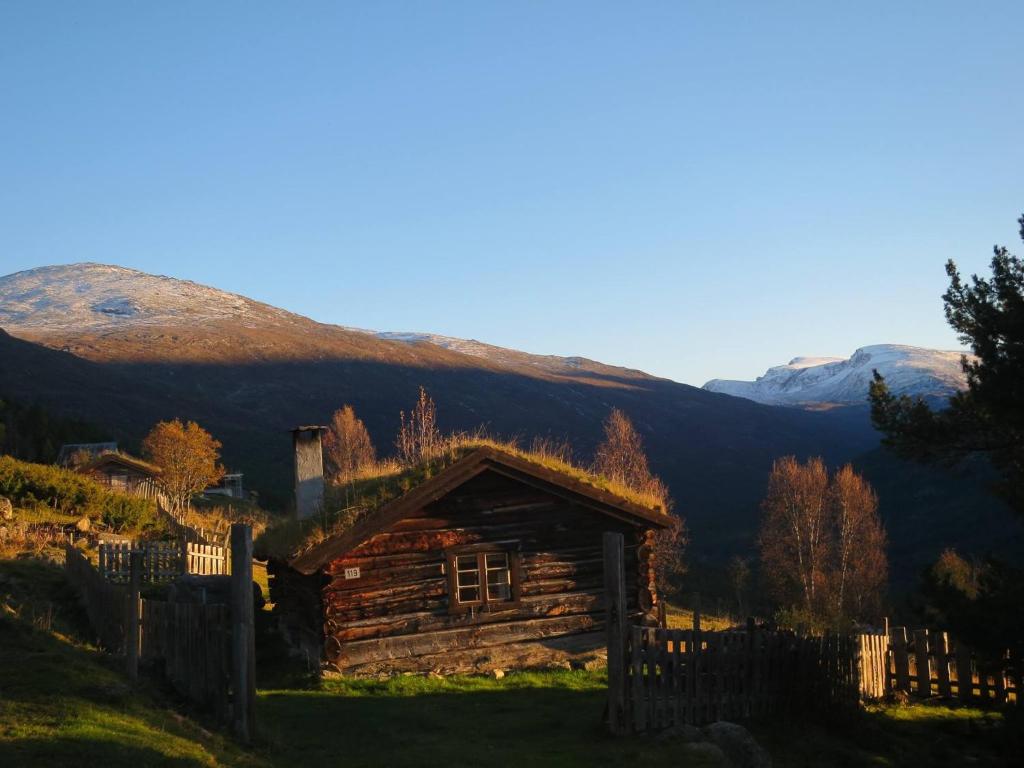uma cabana de madeira com uma cerca e montanhas ao fundo em Strind Gard, Visdalssetra em Boverdalen