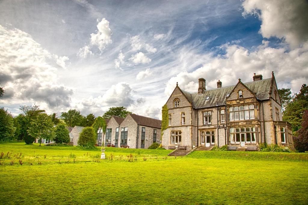 an old house on a green field in front of a building at YHA Castleton Losehill Hall in Castleton