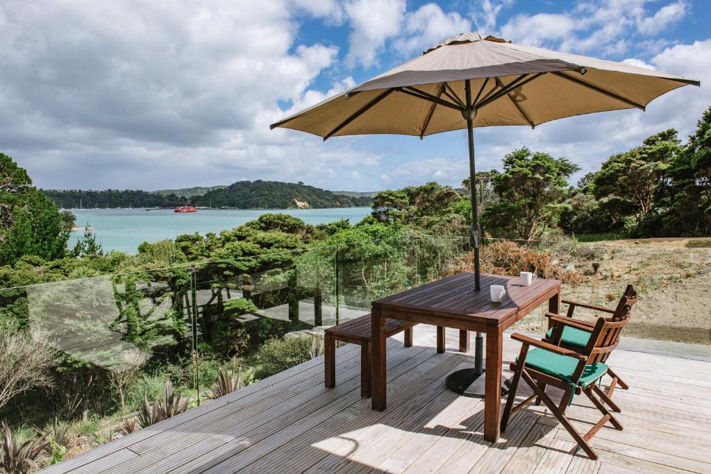 a wooden table and chair with an umbrella on a deck at Te Whau Bach Apartments in Te Whau Bay