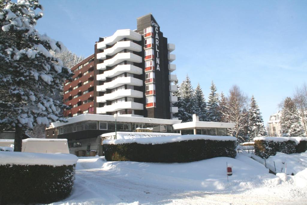 Gran Carlina Hotel في لو مونت دوري: موقف سيارات مغطى بالثلج أمام مبنى