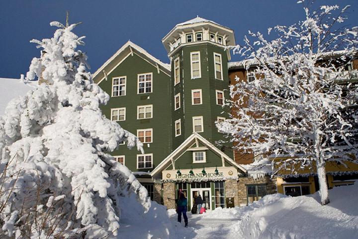 een groot groen gebouw met sneeuw bedekte bomen ervoor bij Highland House in Snowshoe
