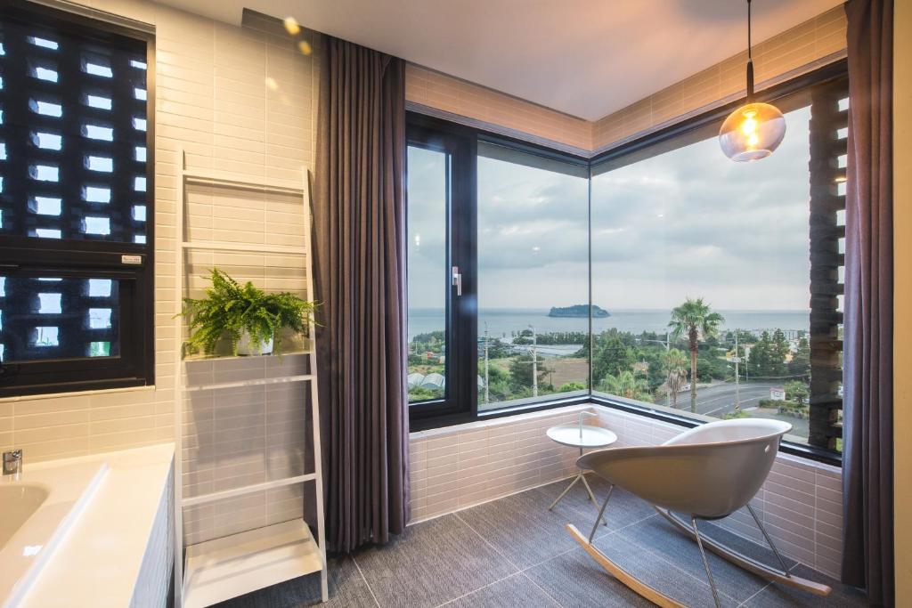 a bathroom with a tub and a chair in front of a window at Jeju Bricks Hotel in Seogwipo