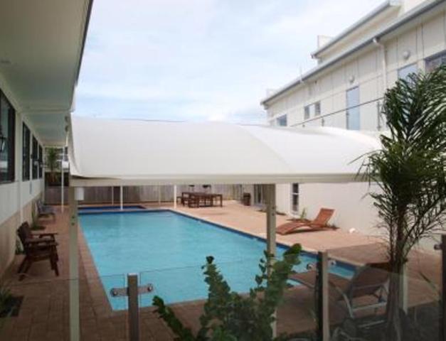 a large swimming pool with a large white umbrella at Albany Rosedale Motel in Auckland