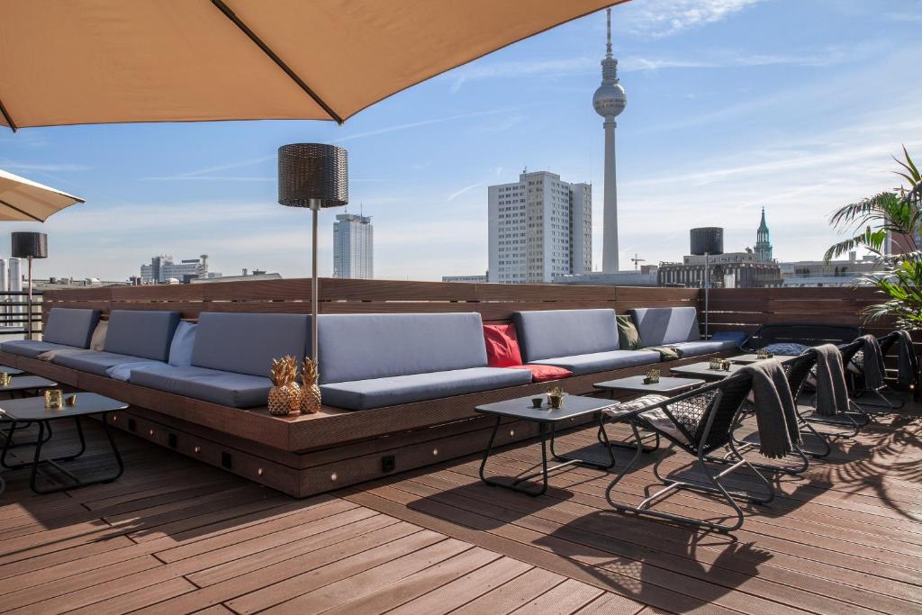a couch on a rooftop with tables and an umbrella at Hotel ZOE by AMANO in Berlin
