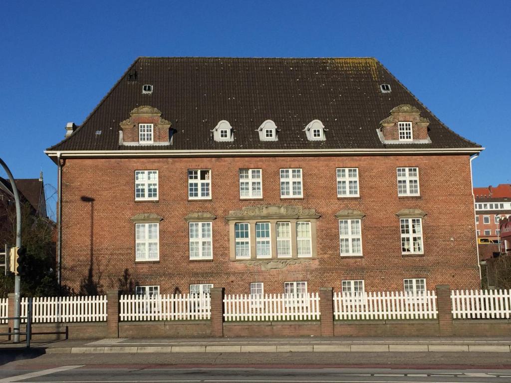 a large red brick building with a white fence at trash de luxe in Schleswig