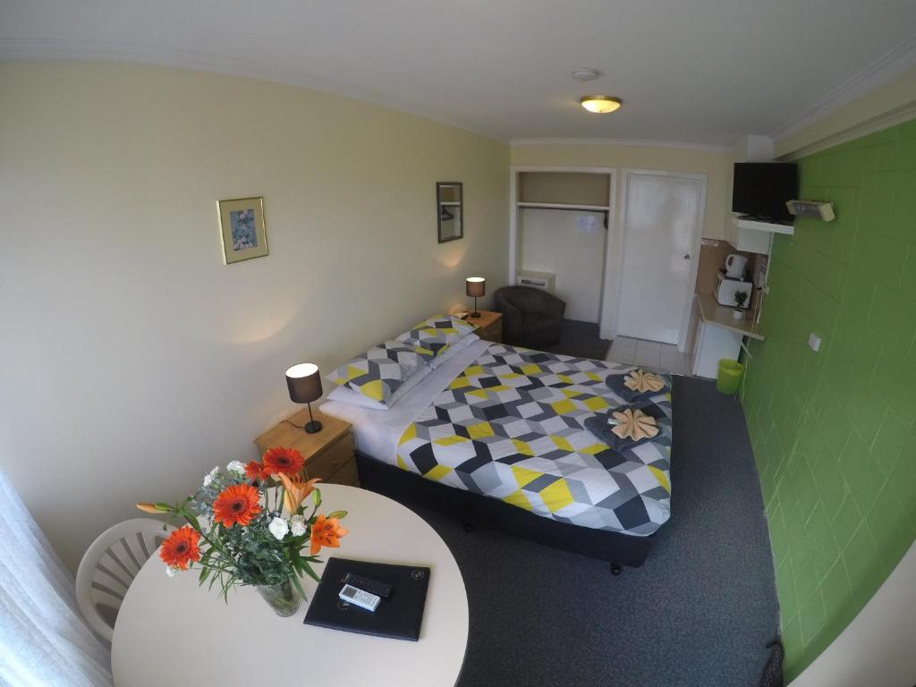 Habitación pequeña con cama y mesa con flores en Turn-in Motel, en Warrnambool
