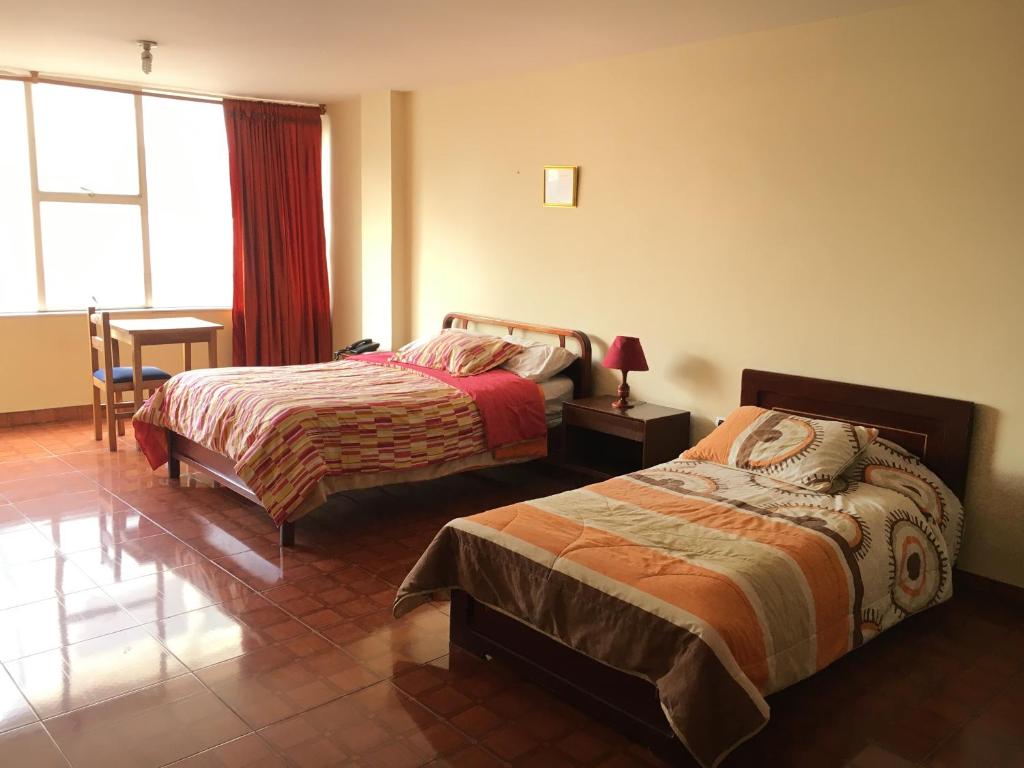 a bedroom with two beds and a desk and a window at Hotel Manila Plaza in Bogotá