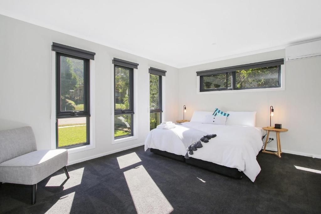 a bedroom with a bed and a chair and windows at Snowgum Bright Retreat - 1 in Bright