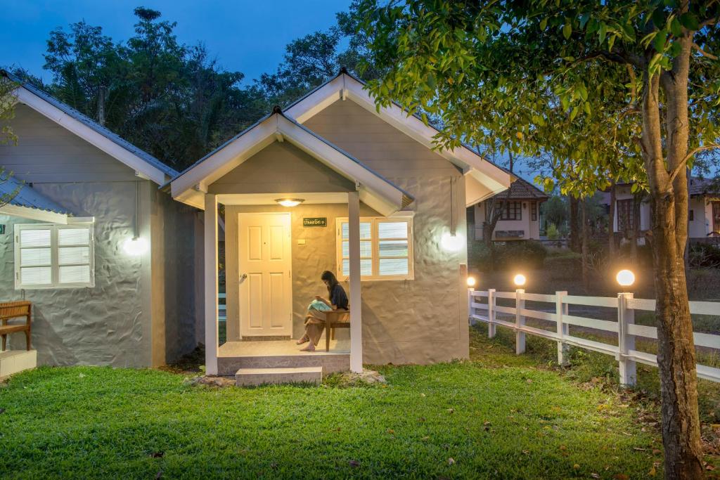 una mujer sentada en el porche de una casita en Ivy Cottage by Qiu, en Saraburi